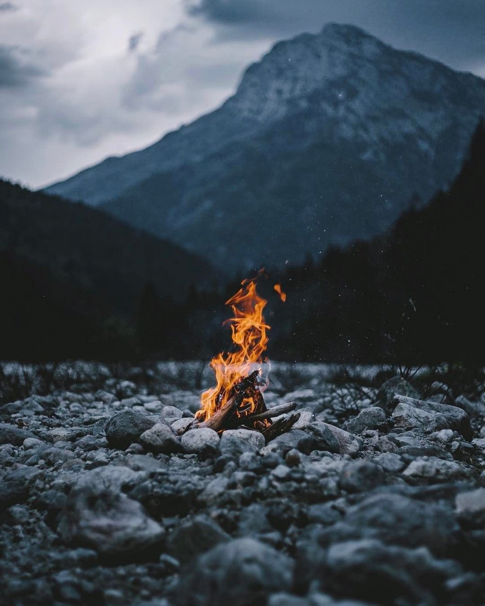 small fire on a rocky shore in front of a mountain